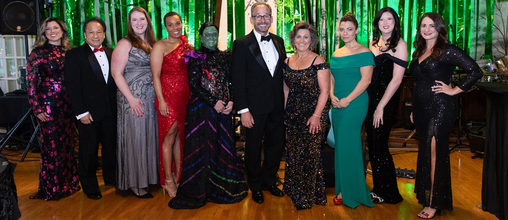 Group of people in formal wear standing in front of a green backdrop.